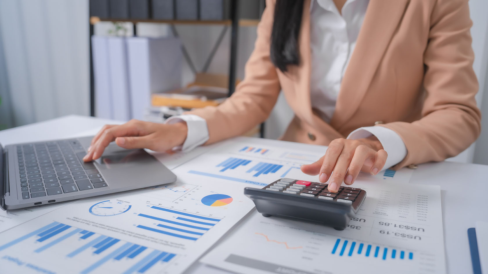 Woman using calculator and laptop on white desk